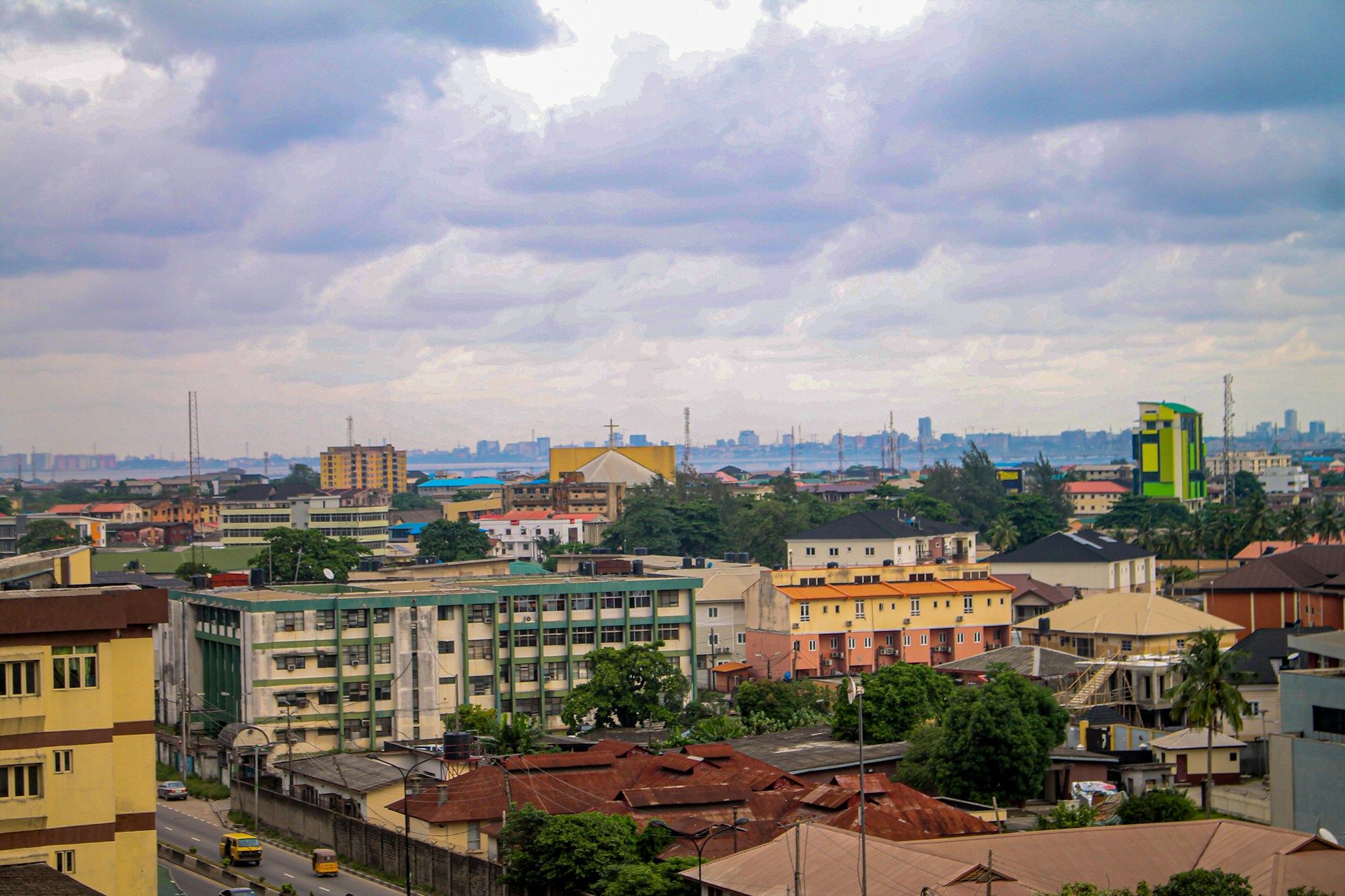 Rooftops and buildings of Yaba in Lagos under a cloudy sky, with the lagoon and the city skyline in the distance.